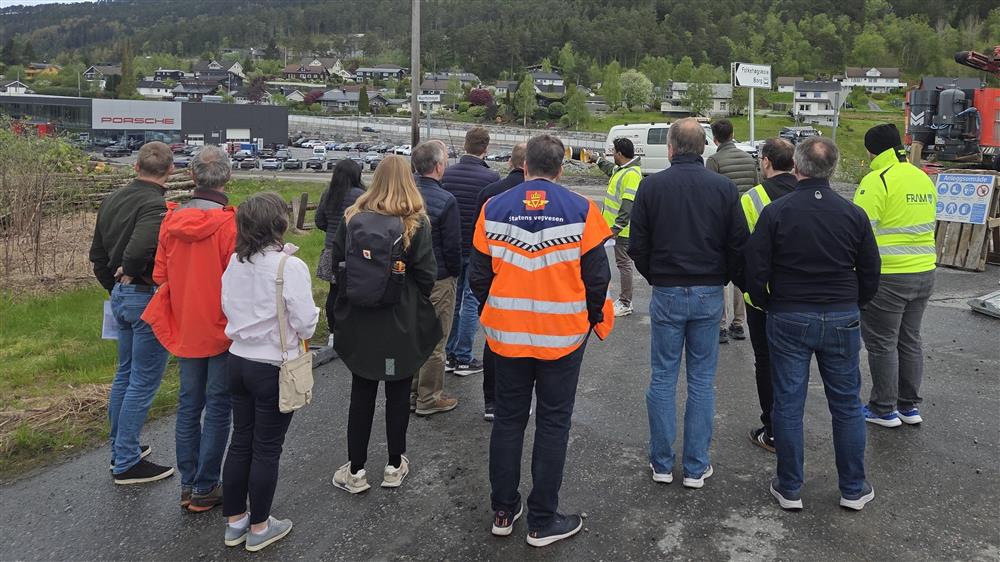 Deltakerne på bussturen står langs veien og ser på prosjektlederen som forteller.  - Klikk for stort bilete